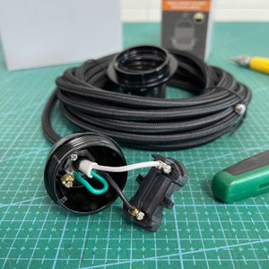 May include: Black electrical cord with a black and white electrical outlet and a green and white wire. The cord is coiled and sitting on a green cutting mat.