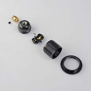 May include: A disassembled black lamp socket with a brass center piece. The socket is made of plastic and has a ribbed design. The socket is in pieces, including the base, the center piece, and the top piece.