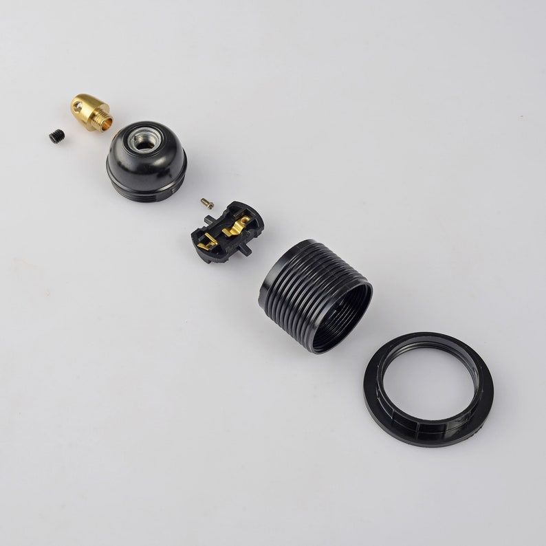 May include: A disassembled black lamp socket with a brass center piece. The socket is made of plastic and has a ribbed design. The socket is in pieces, including the base, the center piece, and the top piece.