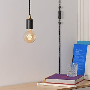 A STEP UP black and gold plug-in pendant light with a globe style Edison light bulb mounted over a table with books.