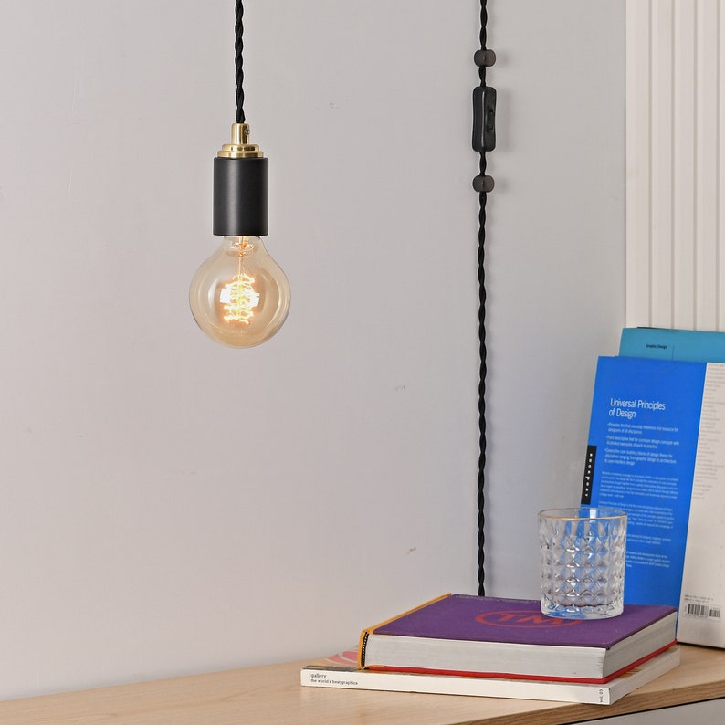 A STEP UP black and gold plug-in pendant light with a globe style Edison light bulb mounted over a table with books.