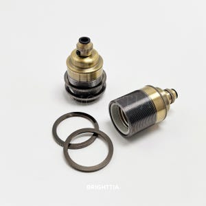 Op de afbeelding: Twee antieke messing en zwarte lamphouders met bijpassende ringen. Eén lamphouder staat rechtop, de andere ligt horizontaal. De ringen zijn donkergrijs. Het woord "BRIGHTTIA" staat onderaan de afbeelding.