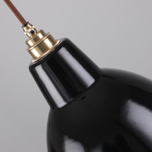 May include: Close-up of a black pendant light fixture with a glossy finish. The light has a brass-colored socket and a brown cord. The design is a classic, industrial style.