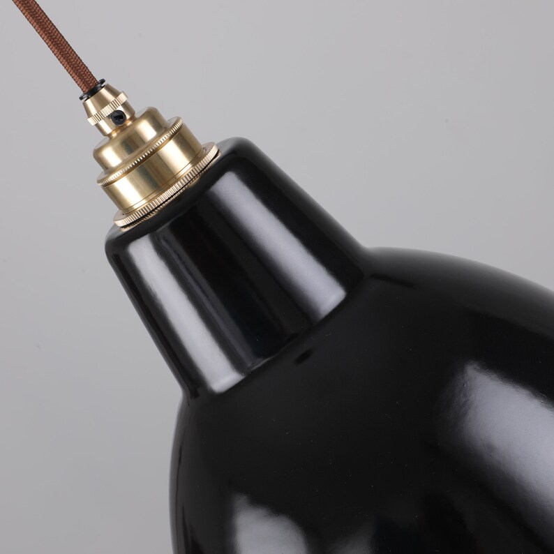 May include: Close-up of a black pendant light fixture with a glossy finish. The light has a brass-colored socket and a brown cord. The design is a classic, industrial style.