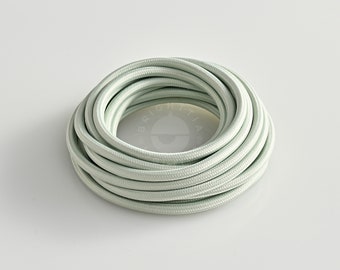 May include: Coiled light green fabric-covered electrical cable. The cable is tightly wound in a circular pattern. The word "BRIGHTTIA" is printed at the bottom of the image.