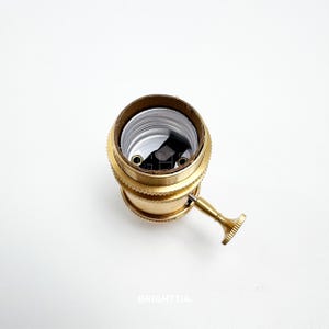 Peut inclure: Un support de lampe en laiton de style vintage avec une finition textur&eacute;e. Il pr&eacute;sente une forme cylindrique avec un int&eacute;rieur marron et un petit levier sur le c&ocirc;t&eacute;. Convient &agrave; divers luminaires.