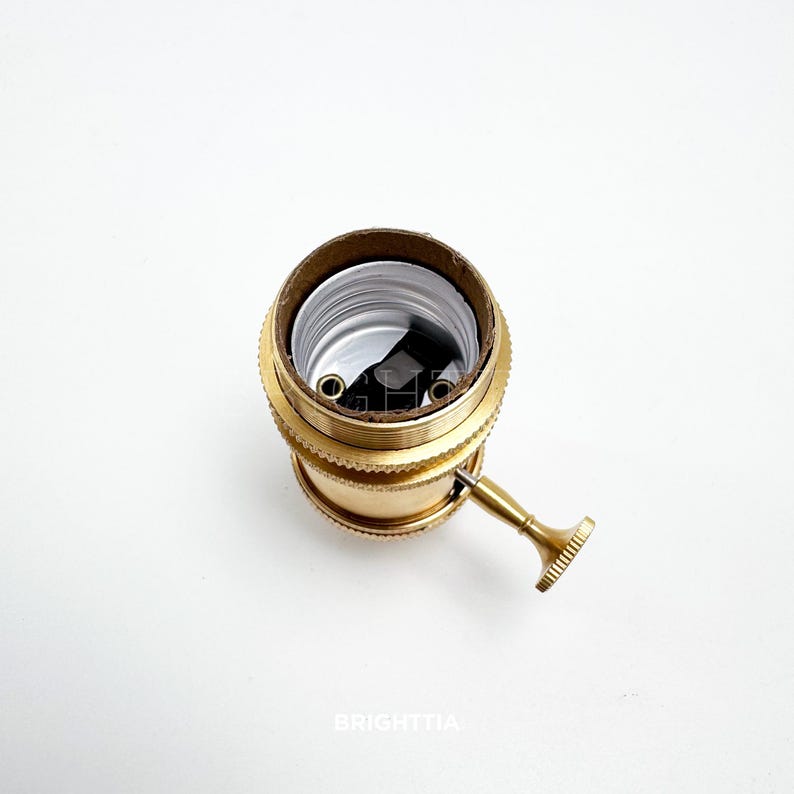 Peut inclure: Un support de lampe en laiton de style vintage avec une finition textur&eacute;e. Il pr&eacute;sente une forme cylindrique avec un int&eacute;rieur marron et un petit levier sur le c&ocirc;t&eacute;. Convient &agrave; divers luminaires.