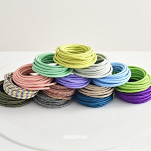 Puede incluir: Una variedad de colores de cable eléctrico, incluyendo verde, azul, rosa, morado y gris. Los cables están enrollados en círculos y apilados uno encima del otro.