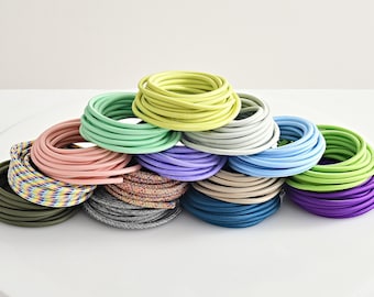Könnte beinhalten: Eine Auswahl an Stromkabeln in verschiedenen Farben, darunter Grün, Blau, Rosa, Lila und Grau. Die Kabel sind zu Kreisen gewickelt und übereinander gestapelt.