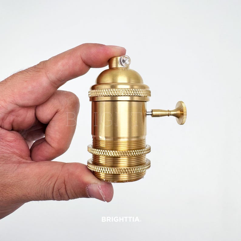 Peut inclure: Un support de lampe de couleur laiton avec un design textur&eacute;. Il comporte un petit cristal transparent sur le dessus et un interrupteur lat&eacute;ral. Le mot "BRIGHTTIA" est imprim&eacute; en bas.