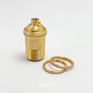 Puede incluir: Un portalámparas de latón con base roscada y tornillo para cableado. Dos anillos de latón a juego están junto al portalámparas. La palabra "BRIGHTTIA" está impresa en la parte inferior.