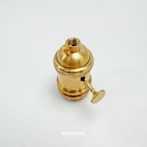 Peut inclure: Un support de lampe de couleur laiton avec un dessus filet&eacute; et un petit interrupteur. Le support a un design textur&eacute; autour de la base et un petit bouton sur le c&ocirc;t&eacute;. Le mot "BRIGHTTIA" est imprim&eacute; en bas.