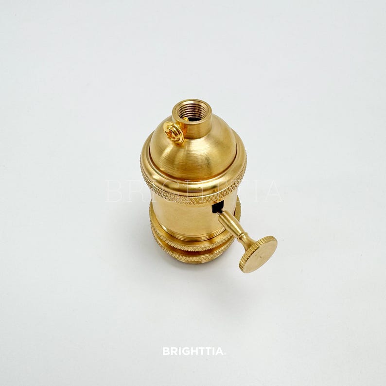 Peut inclure: Un support de lampe de couleur laiton avec un dessus filet&eacute; et un petit interrupteur. Le support a un design textur&eacute; autour de la base et un petit bouton sur le c&ocirc;t&eacute;. Le mot "BRIGHTTIA" est imprim&eacute; en bas.