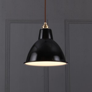 May include: A black pendant light fixture with a glossy finish. The light has a rounded, bell-shaped shade and a white interior. It hangs from a brown cord with a brass-colored fitting at the top. The fixture is designed for overhead lighting.