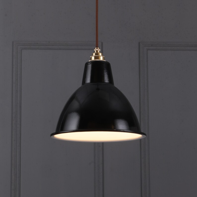 May include: A black pendant light fixture with a glossy finish. The light has a rounded, bell-shaped shade and a white interior. It hangs from a brown cord with a brass-colored fitting at the top. The fixture is designed for overhead lighting.