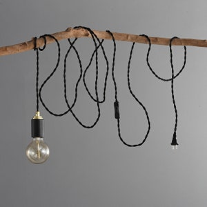 A STEP UP black and gold plug-in pendant light with a globe style Edison light bulb wrapped loosely on a tree branch table with books.