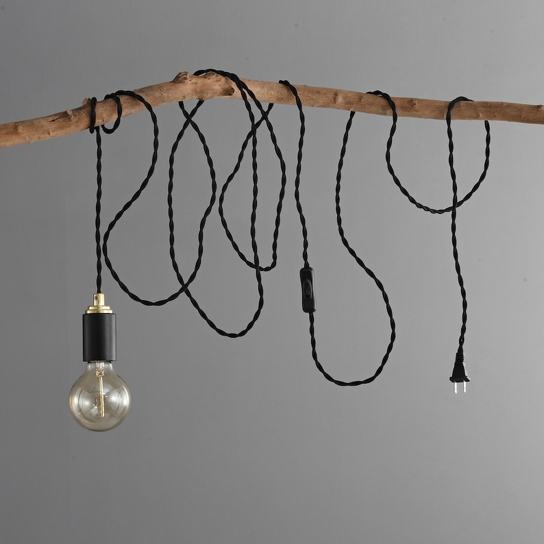 A STEP UP black and gold plug-in pendant light with a globe style Edison light bulb wrapped loosely on a tree branch table with books.