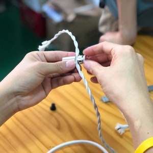 Hand holding and tightening white twisted fabric cord onto aluminum Easy Hook slot.