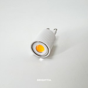 May include: A white LED light bulb with a bright orange center. The bulb has a ribbed design and two metal prongs. The word "BRIGHTTIA" is printed at the bottom.