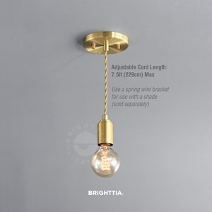 May include: A gold pendant light with a clear glass bulb and a braided cord. The light fixture has a round ceiling mount and a cylindrical base. The cord is adjustable up to 7.5 feet (229 cm). The text "Adjustable Cord Length: 7.5ft (229cm) Max" is visible in the image. The text "Use a spring wire bracket for use with a shade (sold separately)" is also visible in the image.