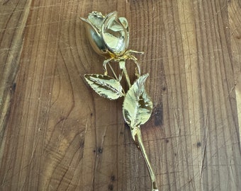 Könnte beinhalten: Eine goldfarbene Rosenbrosche mit einem detaillierten Stiel und Blättern.