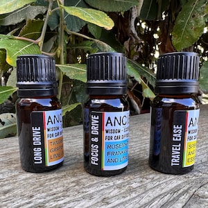 May include: Three small brown glass bottles with black lids and labels. The labels are white with black text and list different essential oil blends for car diffusers. The blends are "Long Drive", "Focus & Drive", and "Travel Ease".