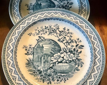 May include: Two antique ceramic plates with a blue and white floral design. The plates feature a detailed illustration of a building, flowers, and birds. The rims have a decorative geometric pattern. The plates are a vintage style.