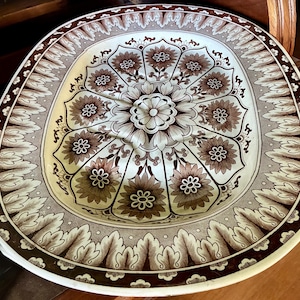 May include: An oval ceramic serving platter featuring a cream-colored base with a dark brown transferware pattern. The design includes a central floral medallion surrounded by radiating flower petals and a wide border of stylized acanthus leaves.
