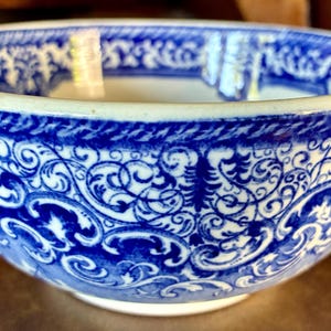May include: A blue and white ceramic bowl with a detailed floral and scrollwork pattern. The bowl has a wide rim and a rounded shape, suitable for serving or display. The design is a classic, timeless style.