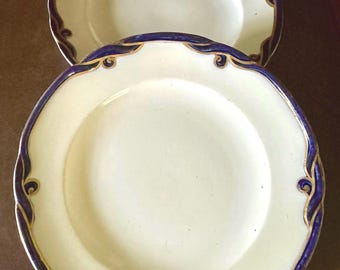 Pode incluir: Dois pratos de cerâmica branca com guarnição azul e dourada. Os pratos têm um design decorativo em torno da borda.