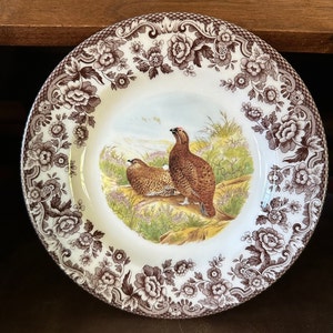 May include: A white ceramic plate with a brown floral border and a central image of two brown birds in a landscape. The plate has a scalloped edge and is likely vintage or antique.