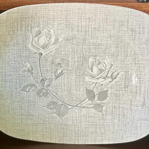 May include: A large, rectangular serving platter with rounded corners. The platter has a light gray textured background with a floral design of two roses and leaves in a lighter gray color. The roses are in full bloom.