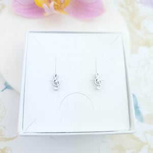 May include: A pair of silver treble clef earrings in a white box. The earrings are small and delicate.