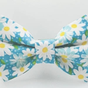 May include: A blue bow tie with a white daisy pattern. The bow tie is made of fabric and has a small, white bow in the center.
