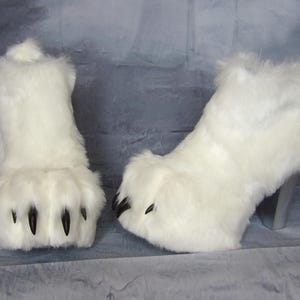 Puede incluir: Un par de botas de piel sint&eacute;tica blanca. Las botas tienen un dise&ntilde;o de pata con garras negras y un tac&oacute;n plateado. Las botas son esponjosas y caprichosas, perfectas para un disfraz o un evento tem&aacute;tico.