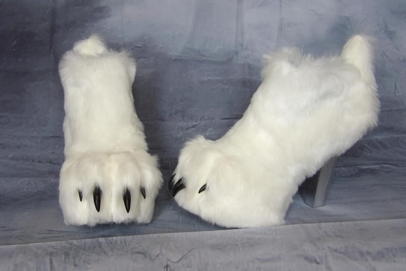 Puede incluir: Un par de botas de piel sint&eacute;tica blanca. Las botas tienen un dise&ntilde;o de pata con garras negras y un tac&oacute;n plateado. Las botas son esponjosas y caprichosas, perfectas para un disfraz o un evento tem&aacute;tico.