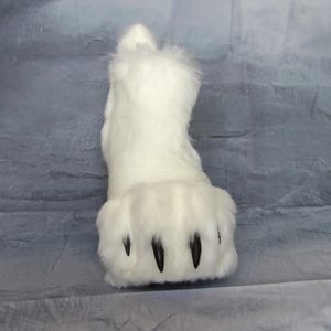 Puede incluir: Una pata de piel sint&eacute;tica blanca con garras negras. El pie peludo tiene forma redondeada y est&aacute; dise&ntilde;ado para parecerse a una pata de animal. El producto es probablemente parte de un disfraz o accesorio de cosplay.