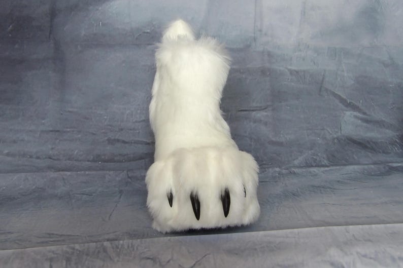 Puede incluir: Una pata de piel sint&eacute;tica blanca con garras negras. El pie peludo tiene forma redondeada y est&aacute; dise&ntilde;ado para parecerse a una pata de animal. El producto es probablemente parte de un disfraz o accesorio de cosplay.