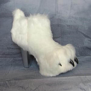 Puede incluir: Una bota de piel sint&eacute;tica blanca con un dise&ntilde;o de pata de oso. La bota tiene un tac&oacute;n plateado y garras negras. La bota est&aacute; dise&ntilde;ada para parecerse a una pata de oso.