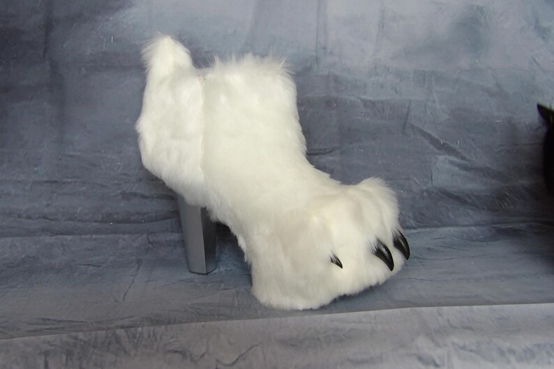 Puede incluir: Una bota de piel sint&eacute;tica blanca con un dise&ntilde;o de pata de oso. La bota tiene un tac&oacute;n plateado y garras negras. La bota est&aacute; dise&ntilde;ada para parecerse a una pata de oso.