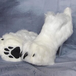 Puede incluir: Pies de disfraz con forma de pata, de piel sint&eacute;tica blanca, con almohadillas y garras negras. La piel sint&eacute;tica es larga y esponjosa, y las patas est&aacute;n dise&ntilde;adas para parecerse a las patas de un animal. Los pies de disfraz son probablemente para cosplay o una mascota.