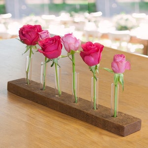 May include: A rustic wooden base with six glass tubes holds a collection of pink and red roses. The roses are arranged in a graduated size order, with the largest rose at the left and the smallest at the right.