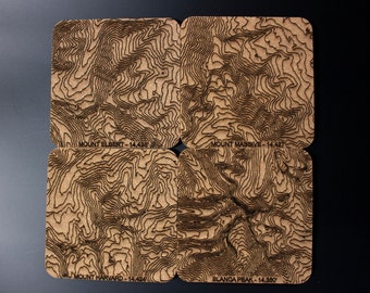 May include: Four wooden coasters with topographic maps of four mountains: Mount Elbert, Mount Massive, Mount Harvard, and Blanca Peak. Each coaster has the mountain name and elevation printed on the bottom.