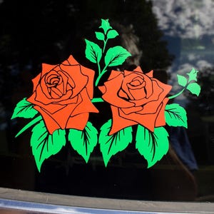 Puede incluir: Una pegatina de dos rosas rojas con hojas y tallos verdes sobre un fondo negro.