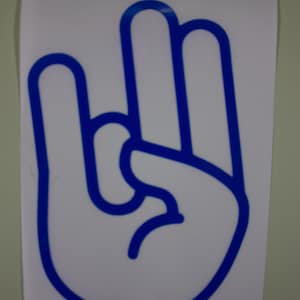 May include: A white rectangular decal featuring a bold blue outline of a hand gesture. The design displays a hand with the thumb and index finger touching to form a circle, while the middle, ring, and pinky fingers are extended upward.