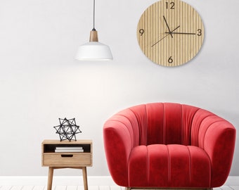 May include: A round wall clock with a light wood grain finish and vertical slats, featuring black numerals at 3, 6, 9, and 12 o'clock, along with black hour, minute, and second hands. The clock is mounted on a plain wall above a red velvet armchair.