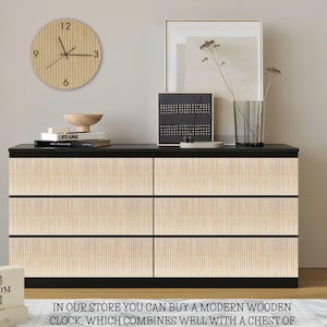 May include: A black six-drawer chest featuring light wood-toned vertical slat overlays on the drawer fronts. A round wooden wall clock with black hands and numbers hangs above. The chest surface holds books, a wooden bowl, and a framed print.