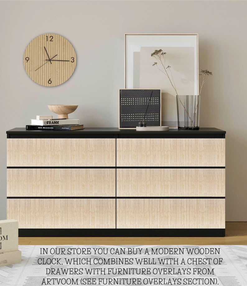 May include: A black six-drawer chest featuring light wood-toned vertical slat overlays on the drawer fronts. A round wooden wall clock with black hands and numbers hangs above. The chest surface holds books, a wooden bowl, and a framed print.