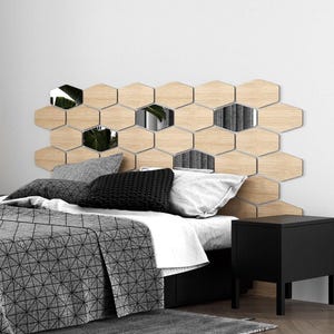 May include: A modern bedroom with a geometric wooden headboard composed of hexagonal panels. Some panels are mirrored, reflecting the room. The bed is made with gray and white bedding, and a black nightstand is visible.