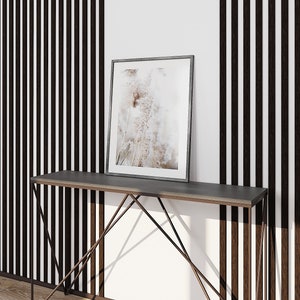 May include: A rectangular picture frame with a thin dark border containing a print of light-colored pampas grass. The frame rests on a slim console table featuring a dark gray top and a geometric metal base with thin, angled support legs.